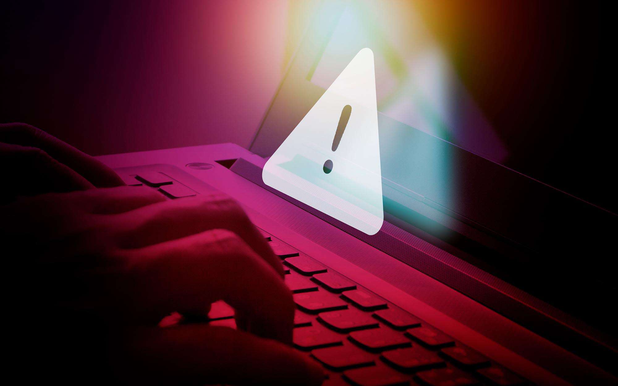 Close-up-of-someones-hands-typing-on-a-laptop-keyboard-with-a-red-color-overlay-and-white-warning-graphic